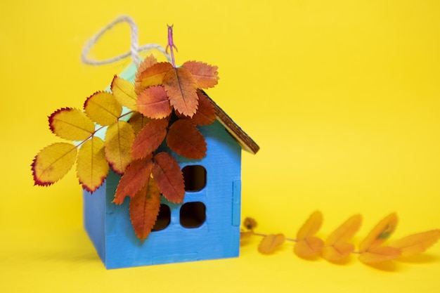 Uma maquete de uma casa de madeira em um fundo amarelo com folhas de outono com um lugar para o seu texto Banner postal