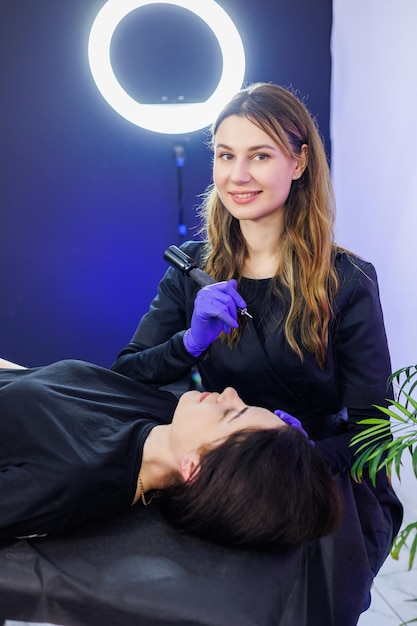Uma maquiadora profissional de maquiagem permanente com uma ferramenta de maquiage permanente Uma jovem maquiadora permanente faz maquiagem de sobrancelha permanente