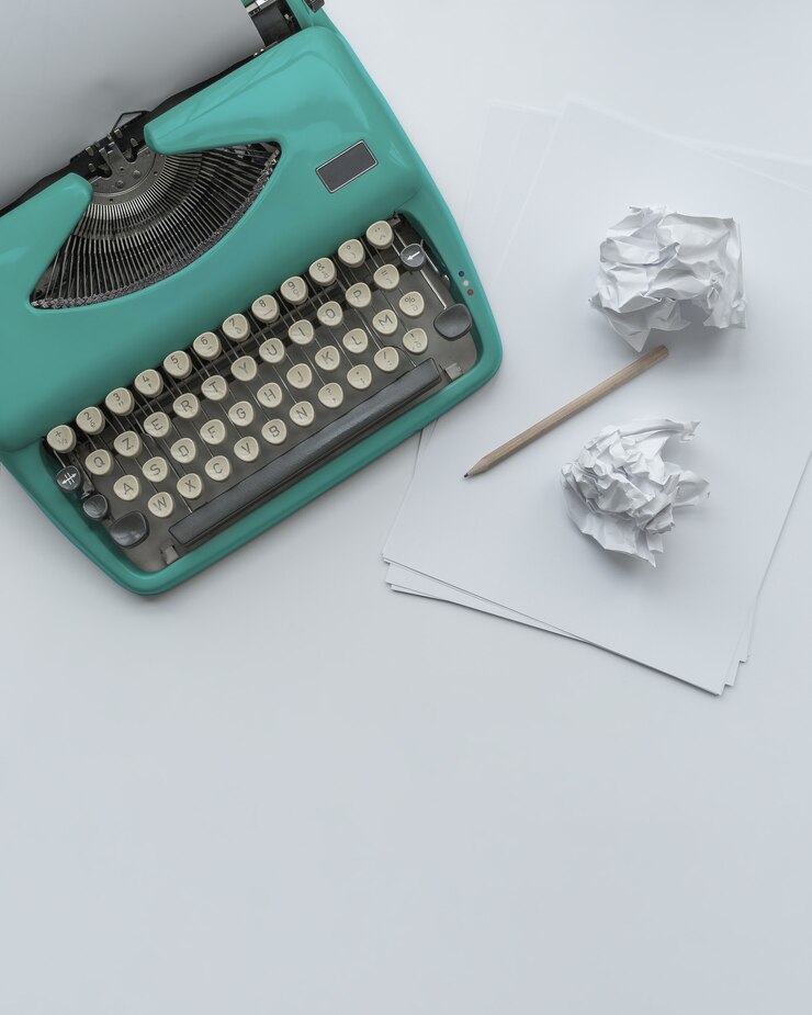 Foto uma máquina de escrever azul vintage com folhas de papel, estêncil e bolas de papel no fundo branco.