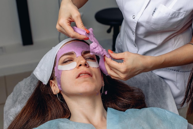 Uma máscara facial congelada é removida de uma jovem. Procedimento de autocuidado. Prestação de serviços de cosmetologia.