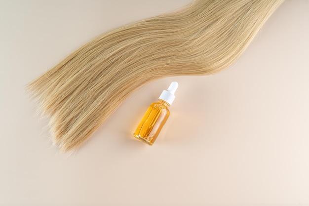 Uma mecha de cabelo loiro alisante e um soro de cuidados com o cabelo sobre um fundo bege Soro ou óleo de perto
