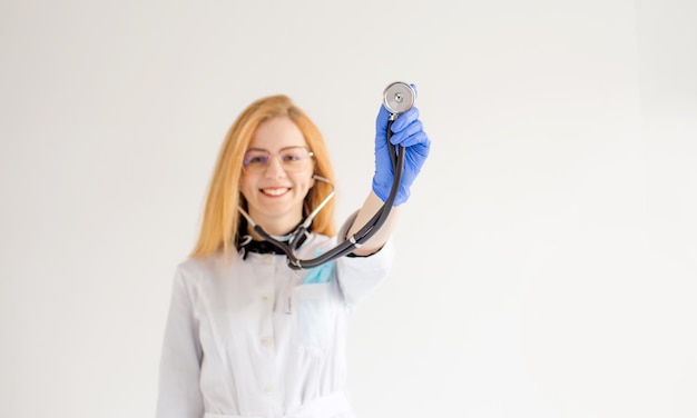 Uma médica com cabelo vermelho segura um estetoscópio nas mãos em um fundo branco isolado