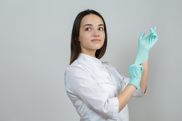 Foto uma médica com luvas de látex e um jaleco branco se prepara para os procedimentos.