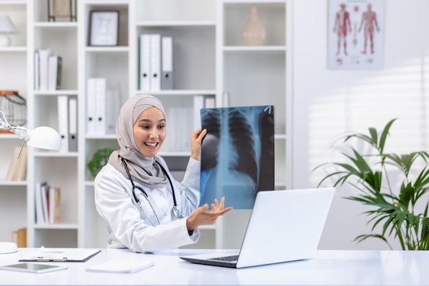 Uma médica de hijab realiza uma consulta on-line em um laptop, mostra raios-x e consulta um paciente