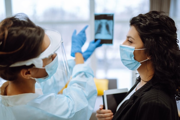 Uma médica em viseira e luvas de proteção examina um raio X de um paciente