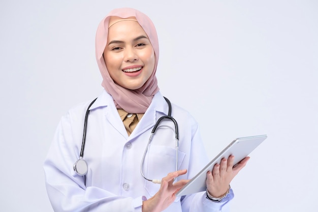 Uma médica muçulmana com hijab sobre estúdio de fundo branco.