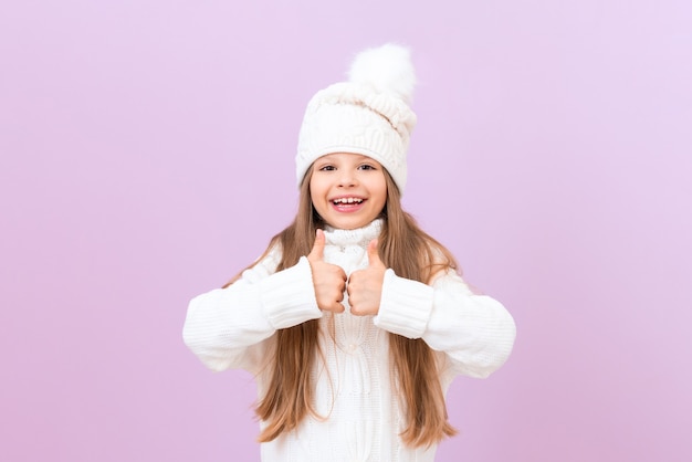 Uma menina alegre com um chapéu quente de inverno mostra os polegares para cima.