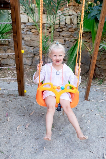 Uma menina alegre e alegre balança em um balanço em uma plataforma de madeira no verão e sorri