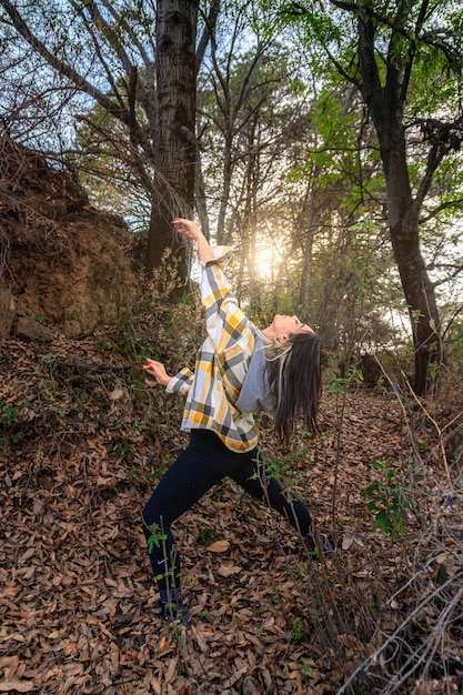 Uma menina alegre no campo dançando impressionantes raios dourados de luz solar brilham