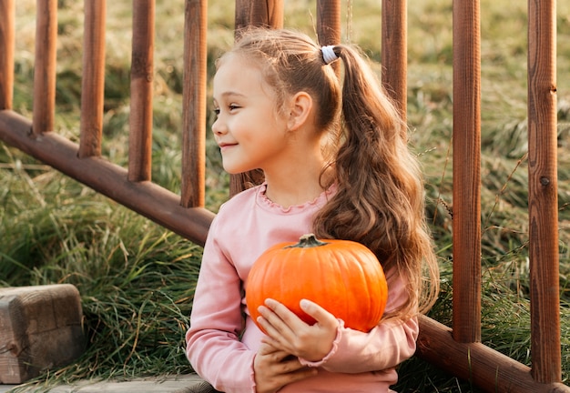 Uma menina alegre segura uma abóbora laranja no parque no outono. Adereços de halloween