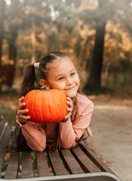 Uma menina alegre segura uma abóbora laranja no parque no outono. Adereços de halloween