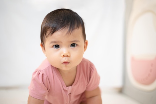 Uma menina asiática de cerca de 1 ano brincando na sala de estar da casa Um bebê fofo vestindo um vestido rosa Fique com os pais em casa