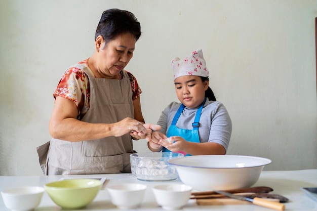 Uma menina asiática e sua avó estão ajudando uma à outra a fazer doces Ela está aprendendo segredos de culinária com sua avó