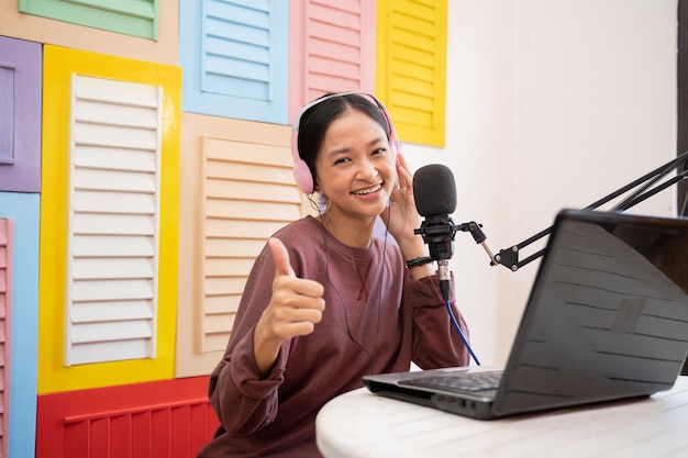 Uma menina asiática falando no microfone enquanto grava o videoblog com o polegar para cima