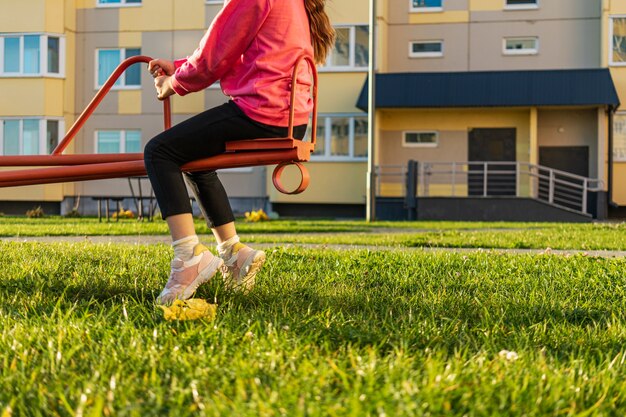 Uma menina balançando em um balanço em um parque infantil no pátio de um prédio de apartamentos. Atividades ao ar livre.