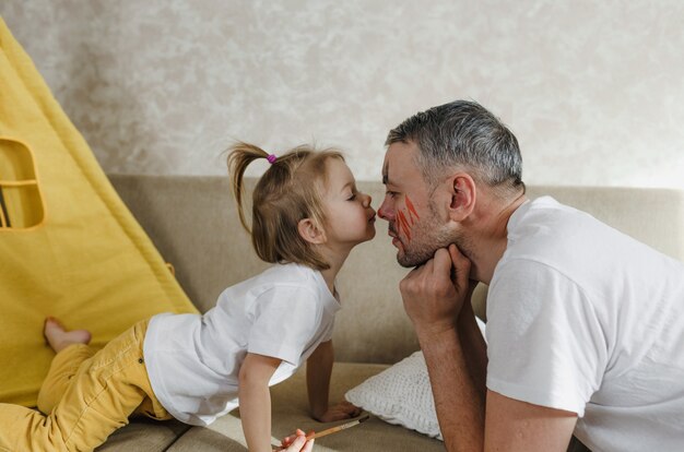 Uma menina beija o nariz do pai enquanto brinca em casa no sofá