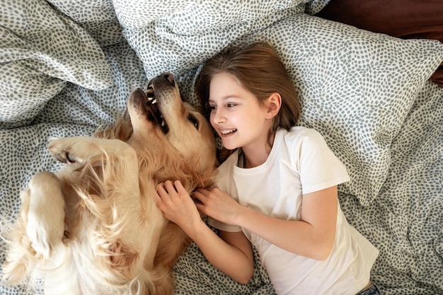 Uma menina bonita a brincar com um cão golden retriever na cama.