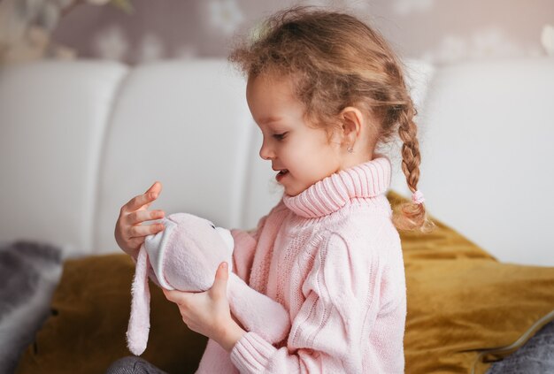 Uma menina bonita acaricia uma lebre de brinquedo. Jogos em casa