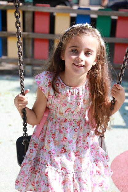 uma menina bonita com cabelos castanhos e olhos verdes claros, feliz e sorrindo em um balanço em Alicante