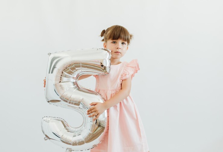 Uma menina bonita comemora seu aniversário de cinco anos. Uma linda criança está usando um vestido rosa