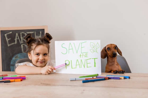 uma menina bonita desenhou um sinal salvar o planeta com seu cachorro dachshund dia da Terra