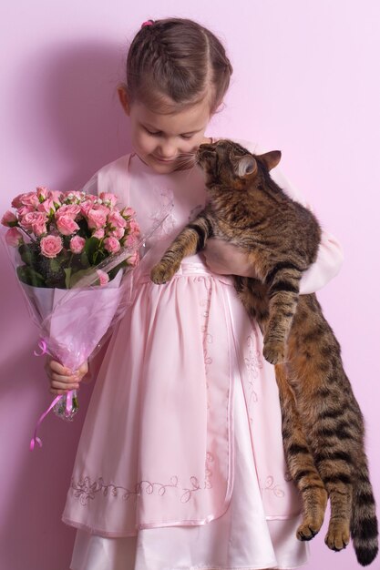 Foto uma menina bonita e um gato em um vestido rosa segura um buquê de rosas rosas