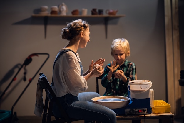 Uma menina bonita e um menino loiro esculpem uma placa na roda de oleiro em um estúdio de arte.
