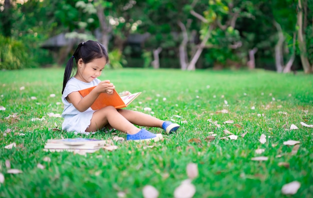 Uma menina bonita em um vestido azul, lendo um livro sentado no parque