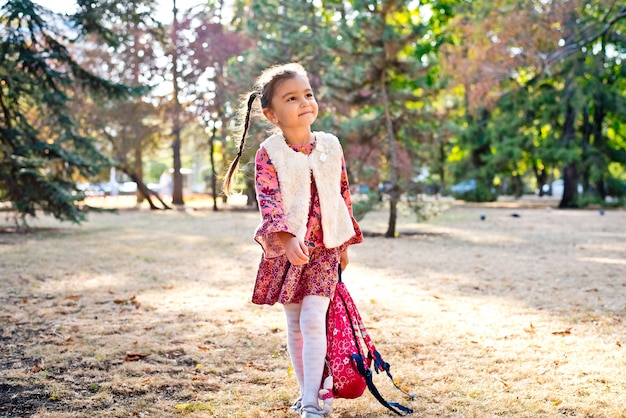 uma menina bonita em um vestido vermelho uma estudante caminha em um parque de outono com uma mochila