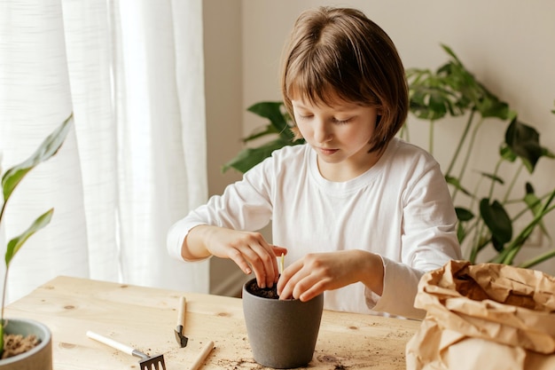 Uma menina bonita está plantando ou transplantando plantas em um vaso de flores em casa.