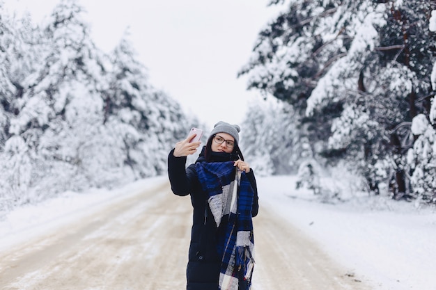 Uma menina bonita faz um selfie no meio de uma estrada de floresta de neve