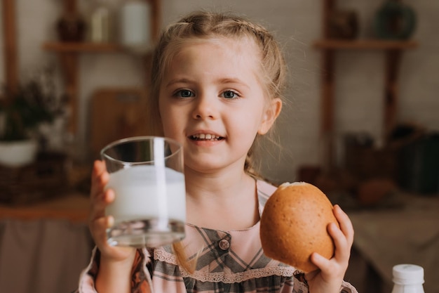 Uma menina bonita na cozinha a beber iogurte e a comer um pão.