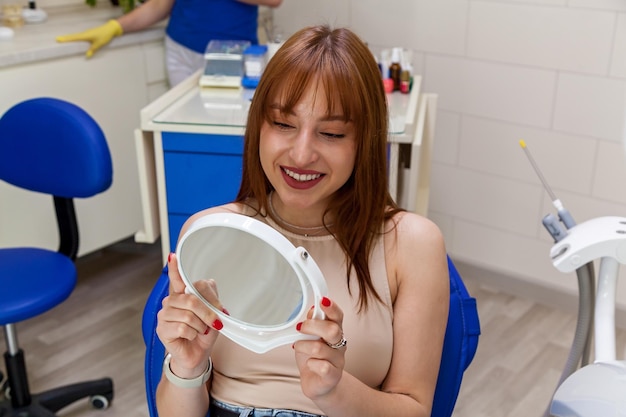 Uma menina bonita sorri ao seu reflexo no espelho Uma menina com belos dentes brancos sorri depois de um tratamento no dentista