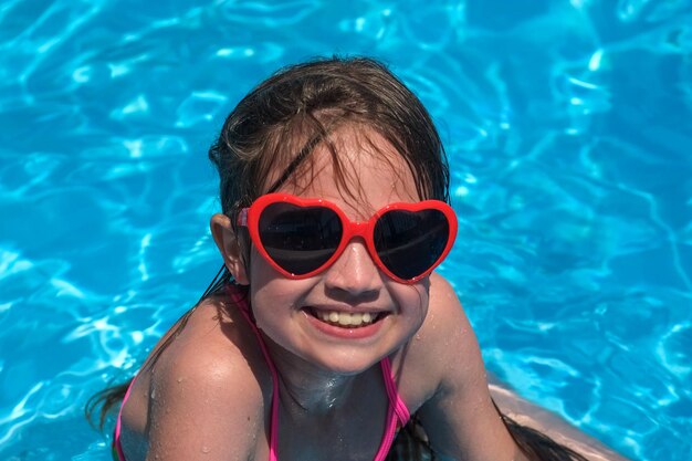 Foto uma menina bonita sorridente com óculos de sol em forma de coração na piscina num dia ensolarado