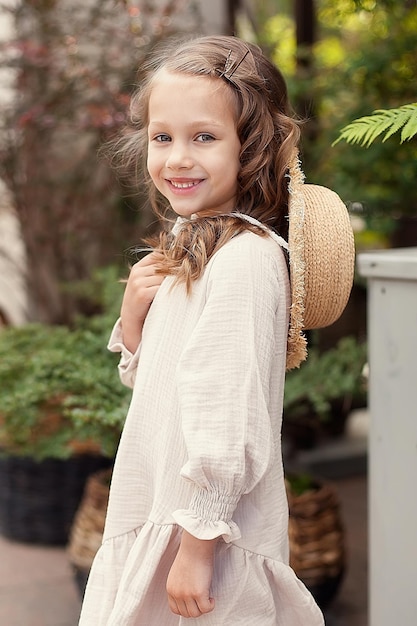 Uma menina bonitinha com um chapéu de palha na rua em um dia de verão no parque em um fundo de flores A criança olha para a câmera Infância feliz Um passeio ao ar livre