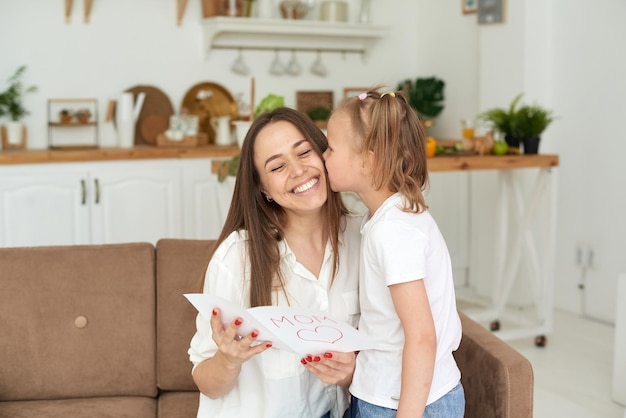 Uma menina bonitinha dá à mãe um cartão de felicitações para o dia das mães ou 8 de março