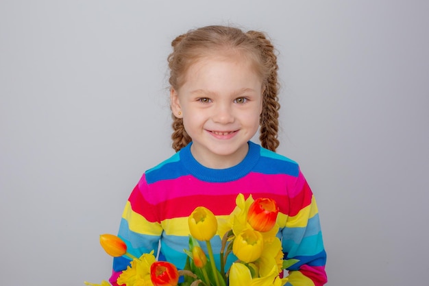 Uma menina bonitinha em um suéter multicolorido segura um buquê de flores da primavera em um fundo branco