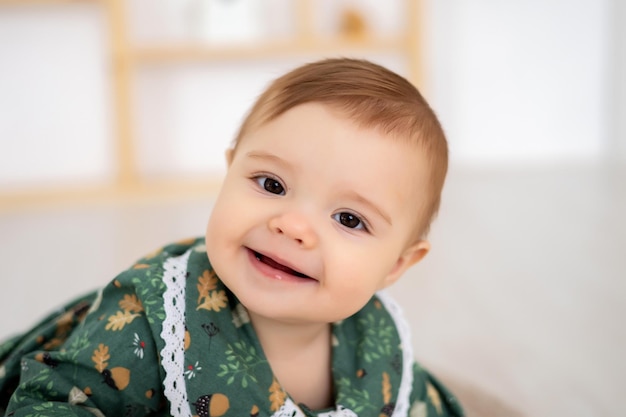 Uma menina bonitinha em um vestido de algodão verde está sentada em um tapete no quarto das crianças em casa olhando para a câmera sorrindo um grande retrato