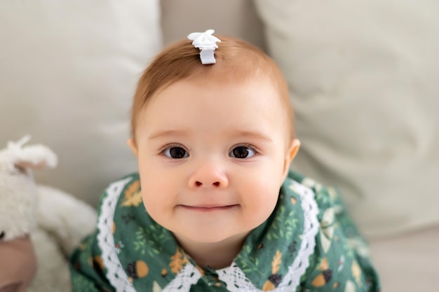 Uma menina bonitinha em um vestido de algodão verde está sentada no sofá na sala de estar da casa olhando para a câmera sorrindo um grande retrato