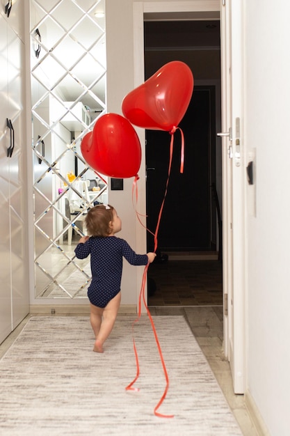 Uma menina bonitinha está brincando com uma bola vermelha em forma de coração Lindo cartão postal de presente