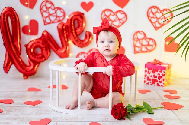 uma menina bonitinha está sentada em uma roupa vermelha contra um fundo de corações vermelhos e o amor de inscrição. o conceito de dia dos namorados, dia dos namorados