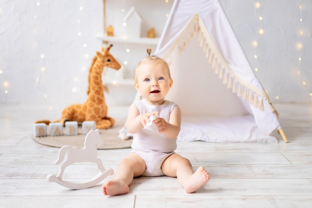 Uma menina bonitinha está sentada em uma sala de jogos infantil aconchegante e brilhante Têxteis para crianças para o berçário Uma criança feliz