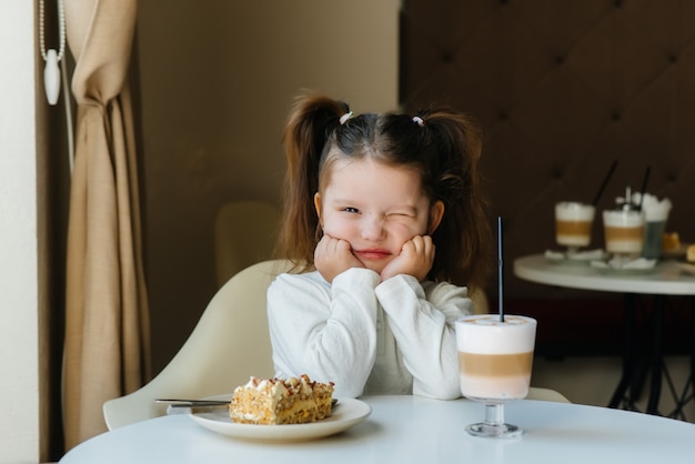 Uma menina bonitinha está sentado em um café e olhando para um bolo e cacau close-up. dieta e nutrição adequada.