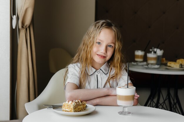 Uma menina bonitinha está sentado em um café e olhando para um bolo e cacau close-up. dieta e nutrição adequada.