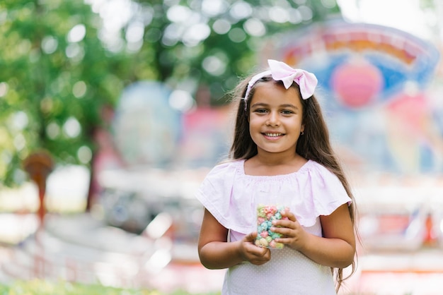 Uma menina bonitinha no parque no verão está segurando pipoca nas mãos e sorrindo com um sorriso largo