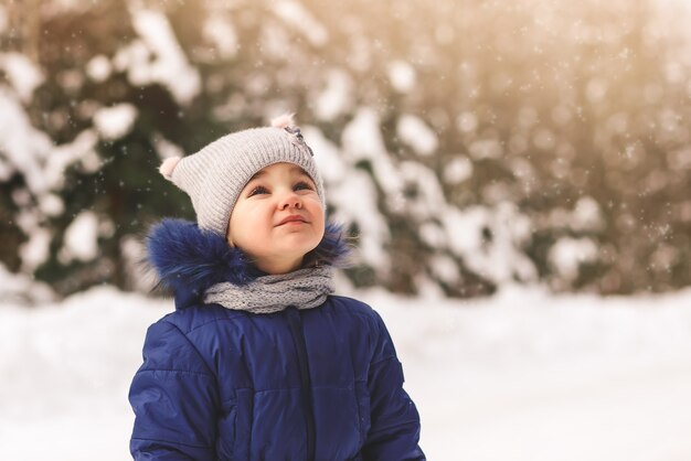 Uma menina bonitinha olha para a neve no inverno na rua