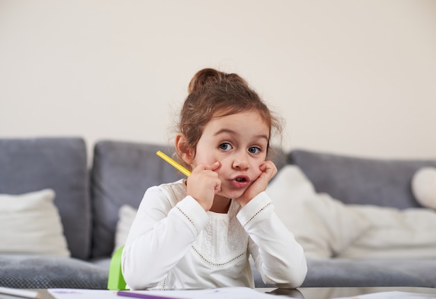 Uma menina bonitinha sentada à mesa com uma caneta amarela nas mãos