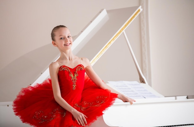 Uma menina bonitinha sonha em se tornar uma bailarina profissional Em uma sala branca, ele fica ao piano em um pacote vermelho brilhante Estudante de escola profissional