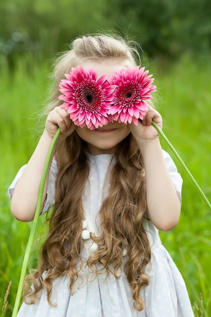 Foto uma menina brinca com gerberas vermelhas e fecha os olhos com elas.