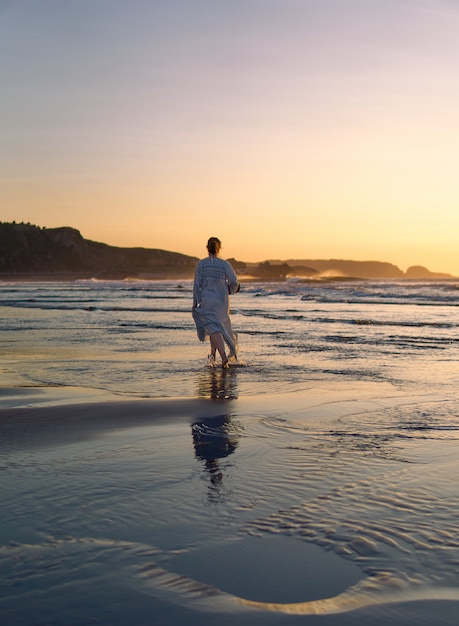 Uma menina caminhando ao longo da costa de uma praia na hora de ouro